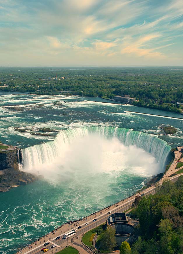 Aerial view of the Canadian Horseshoe Falls on a summer day with a blue sky and green trees in the foreground