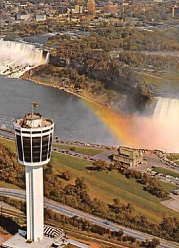 A stunning aerial view of Niagara Falls with a vibrant rainbow arching over the cascading water, Tower Hotel overlooking the scenery.