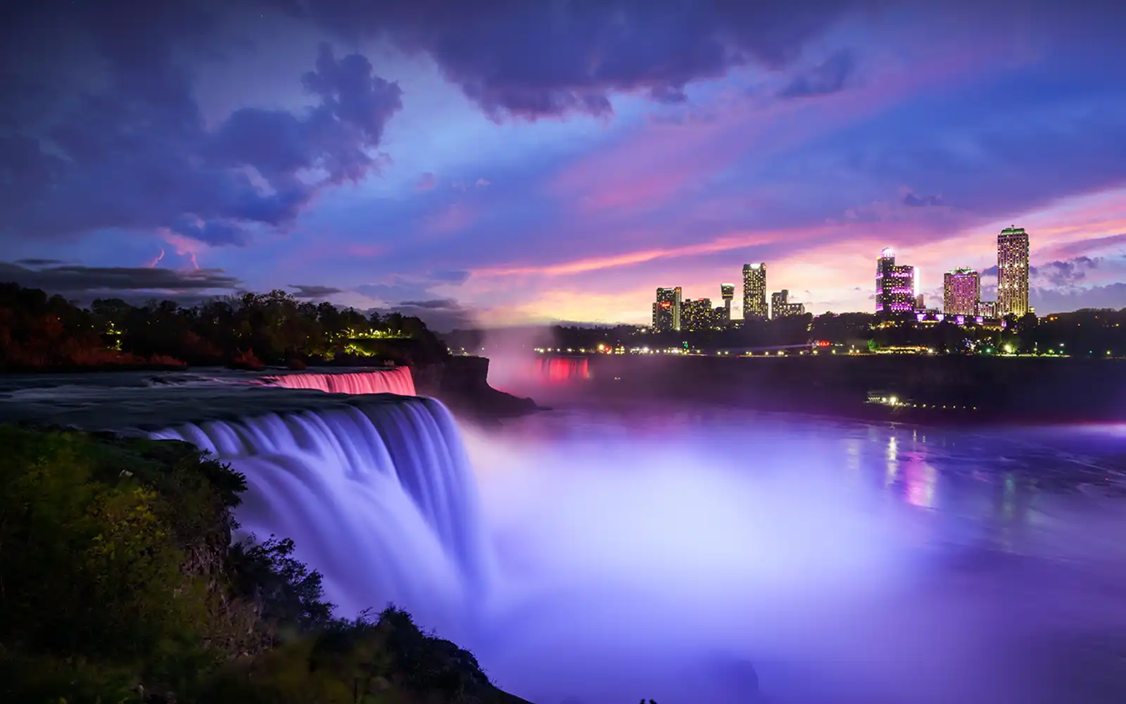 Nighttime view of Niagara Falls, brightly lit with water flowing under dark sky.
