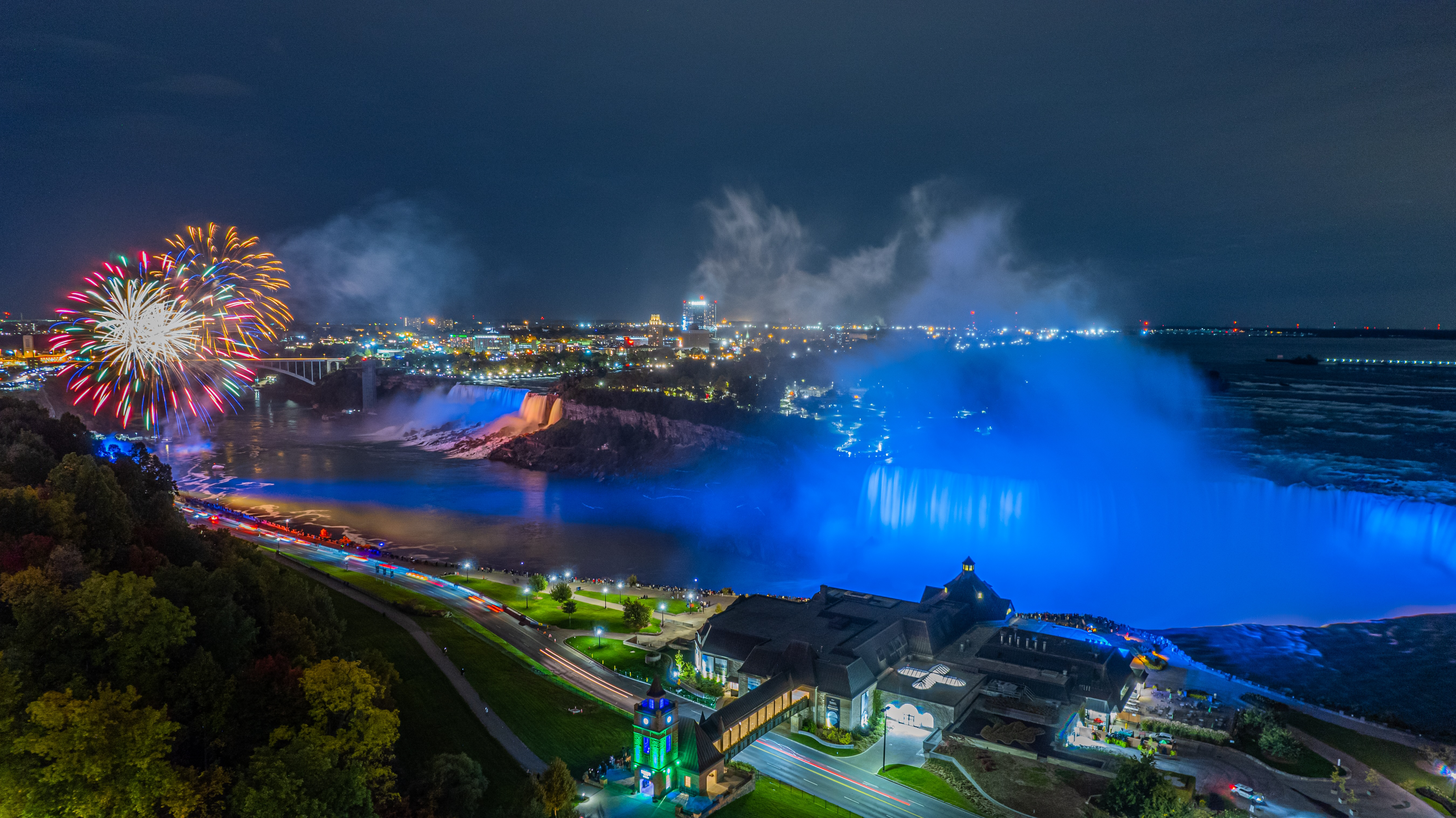 A stunning aerial view of Niagara Falls with a vibrant rainbow arching over the cascading water, Tower Hotel overlooking the scenery.
