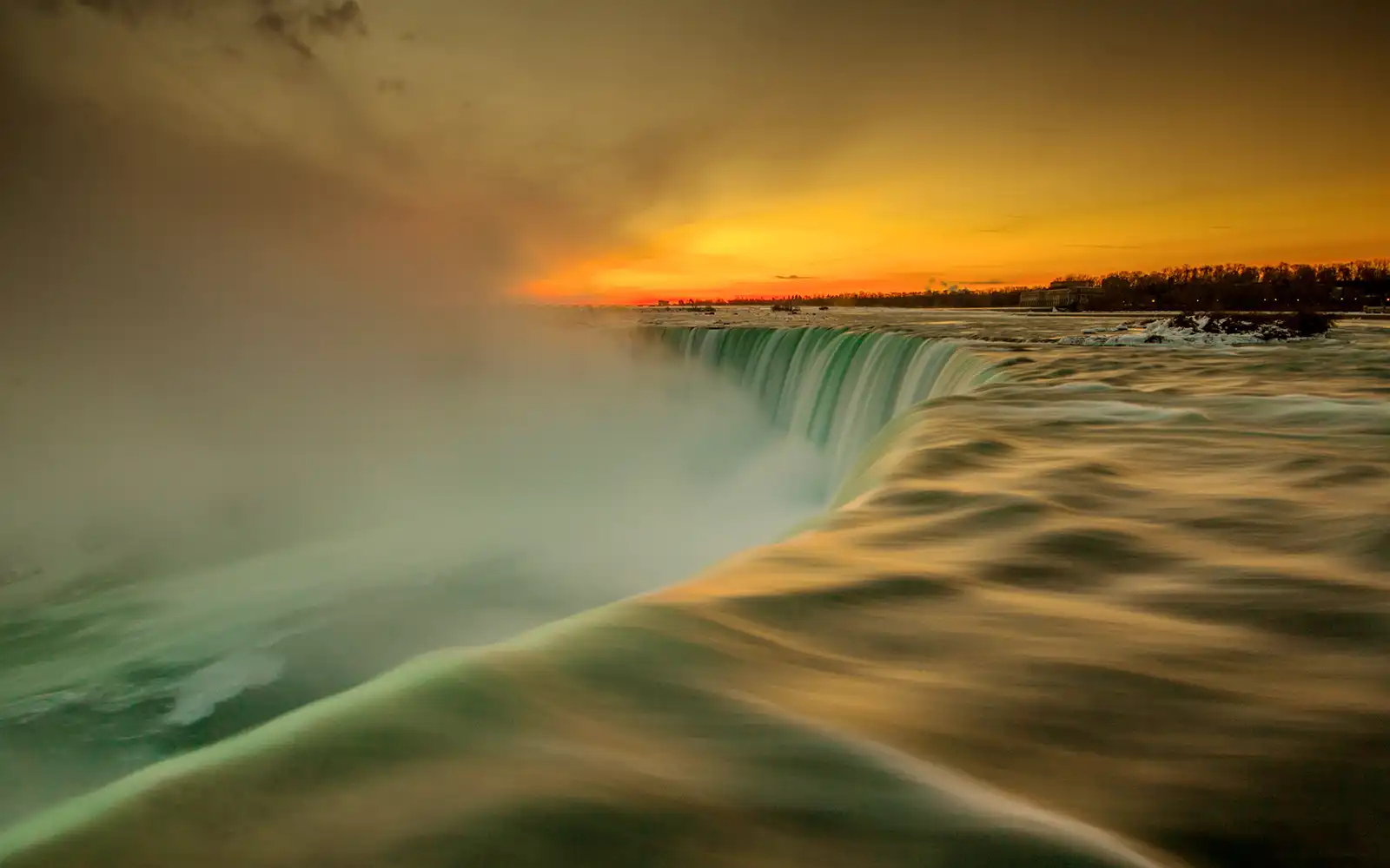 Close up of Niagara Falls' cascading water with sky glowing with an orange sunset.